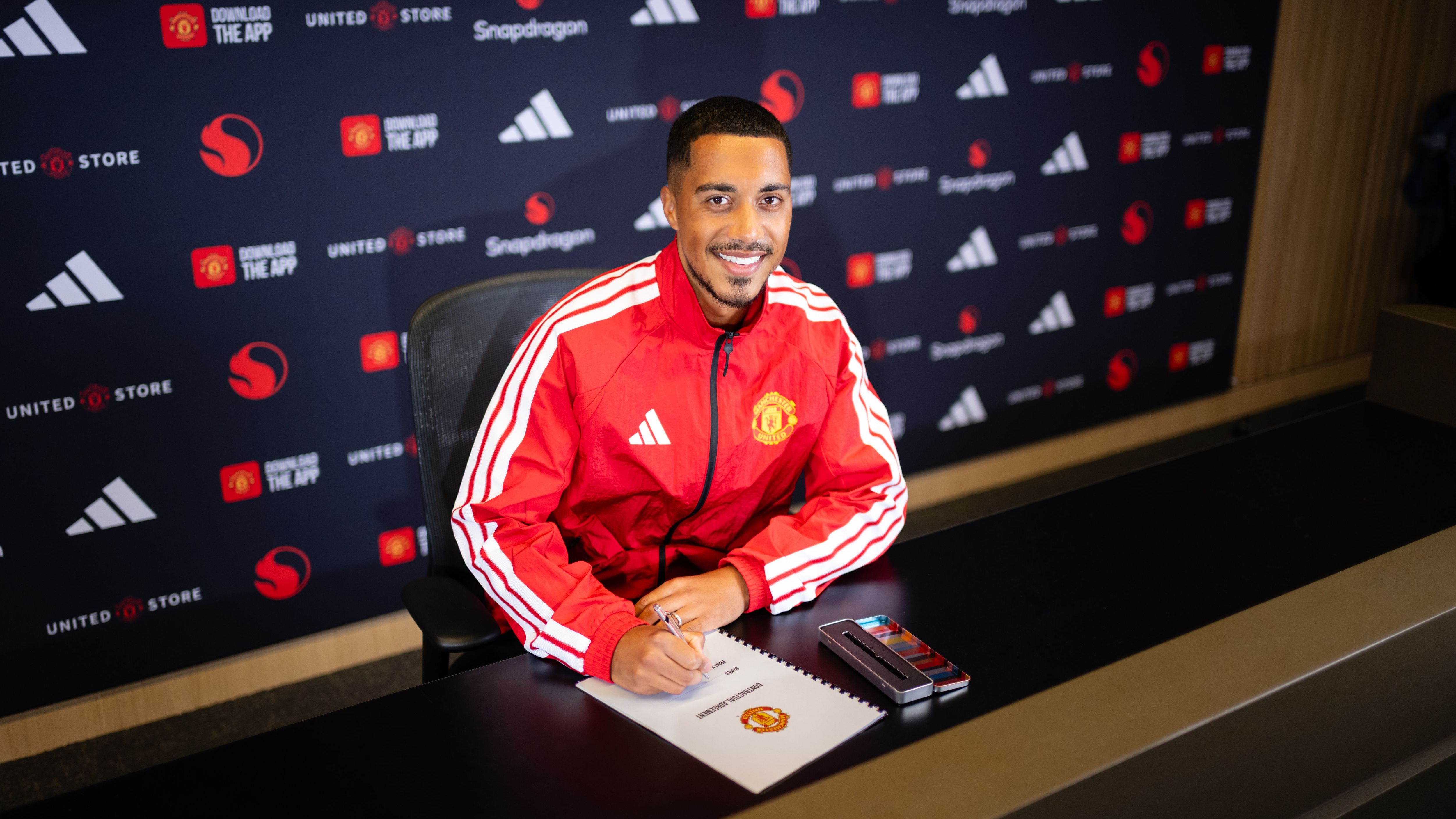 Youri Tielemans tersenyum dengan latar belakang logo Manchester United